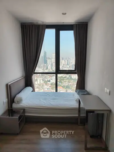 Compact bedroom with stunning city view through large window, modern furnishings, and natural light.