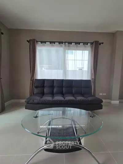 Modern living room with sleek black sofa and glass coffee table, featuring elegant curtains and neutral tones.