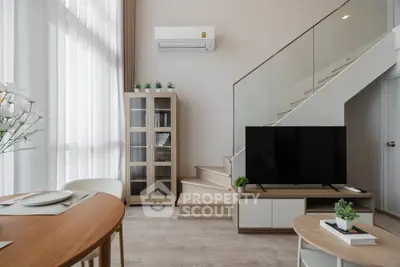 Modern living room with stylish furniture and staircase, featuring a sleek TV setup and natural light.