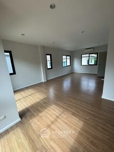 Spacious empty room with wooden flooring and ample natural light from multiple windows.