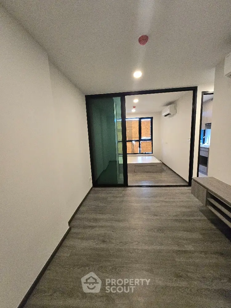 Modern apartment interior with sleek flooring and glass partition, featuring air conditioning and ample natural light.