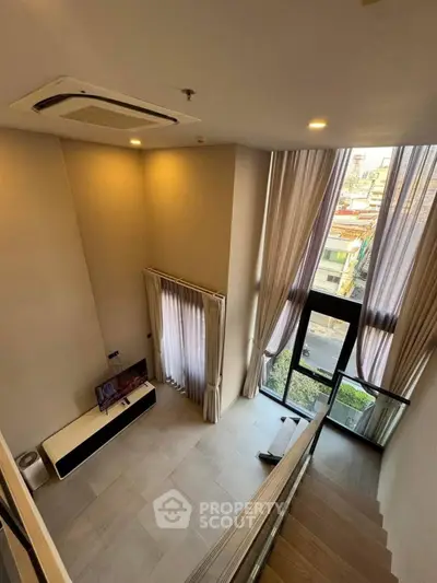 Spacious modern living room with high ceilings and large windows offering city views.