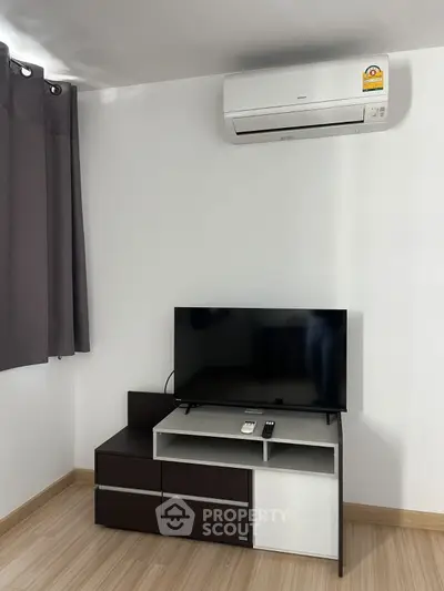 Modern living room with air conditioner and TV setup on wooden floor.