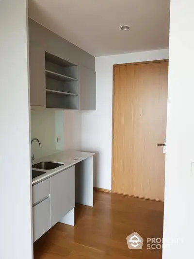 Compact modern kitchen with sleek white cabinetry and built-in shelving, complemented by warm wooden flooring, offering a cozy culinary space.