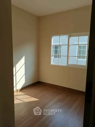 Bright empty room with wooden flooring and large window, perfect for customization.