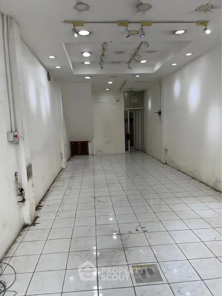 Spacious empty commercial space with tiled flooring and recessed lighting, ideal for retail or office setup.