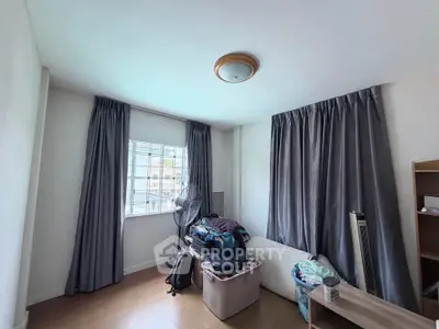 Cozy bedroom with natural light, wooden flooring, and modern curtains, perfect for a comfortable living space.