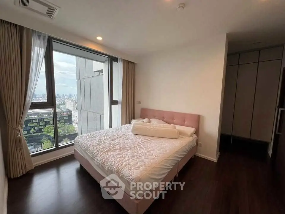 Spacious bedroom with large window offering stunning city views and elegant decor.