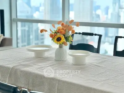 Elegant dining area with city view, featuring a stylish table setting and vibrant floral centerpiece.