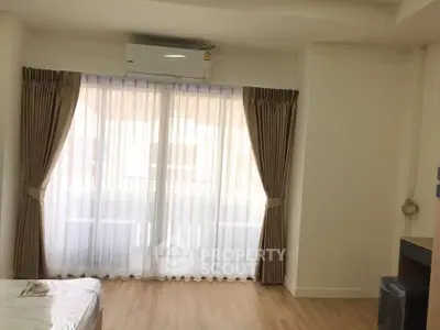 Bright bedroom with large window and elegant curtains, featuring wooden flooring and air conditioning.