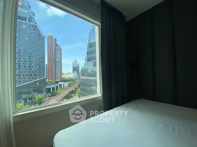Modern bedroom with stunning city view through large window, featuring sleek urban architecture.