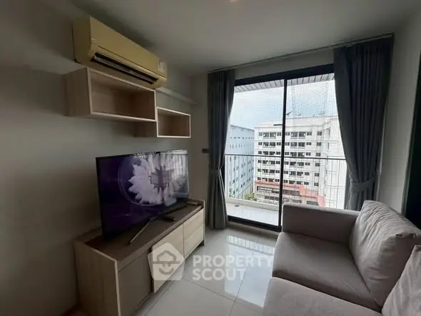 Modern living room with large TV, cozy sofa, and balcony view in urban apartment.