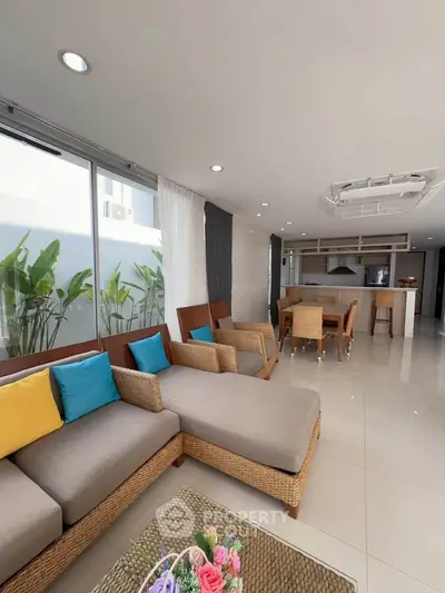 Spacious modern living room with open kitchen, featuring stylish furniture and large windows for natural light.
