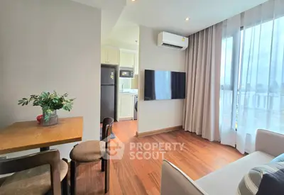 Modern living room with hardwood floors, wall-mounted TV, and open kitchen layout in a bright apartment.