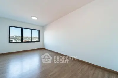 Spacious empty room with wooden flooring and large window view.