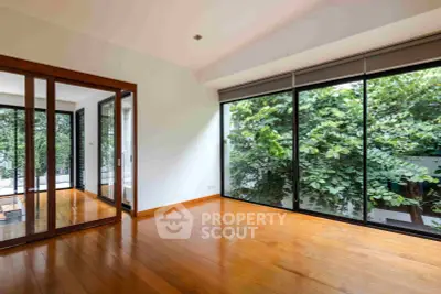 Spacious living room with large windows and lush garden view, featuring elegant wooden flooring.
