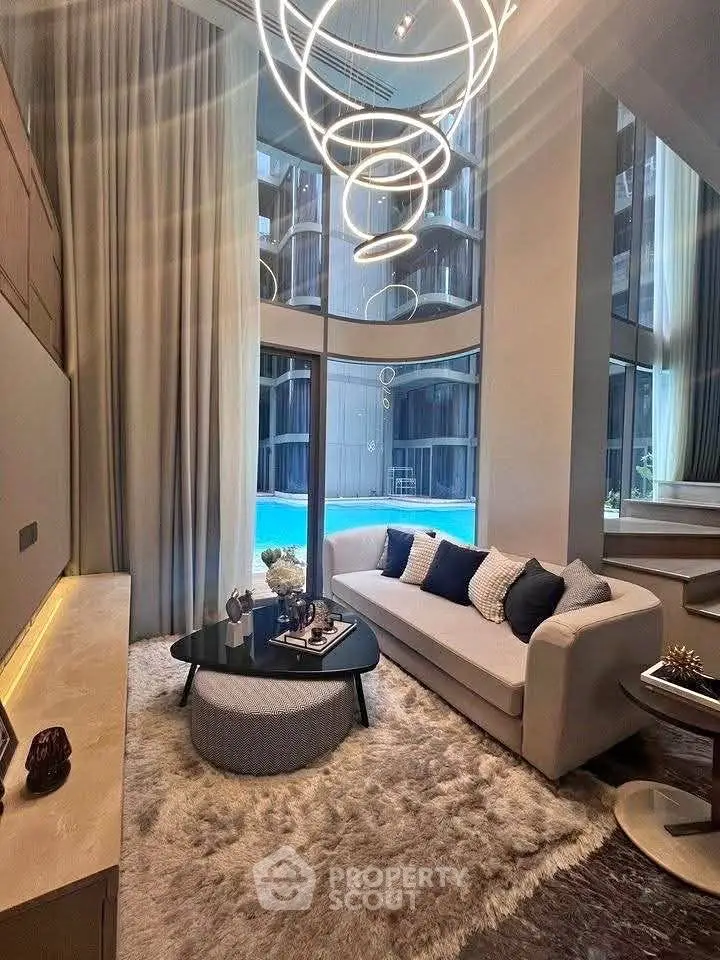 Luxurious living room with modern chandelier and pool view, featuring elegant decor and plush furnishings.