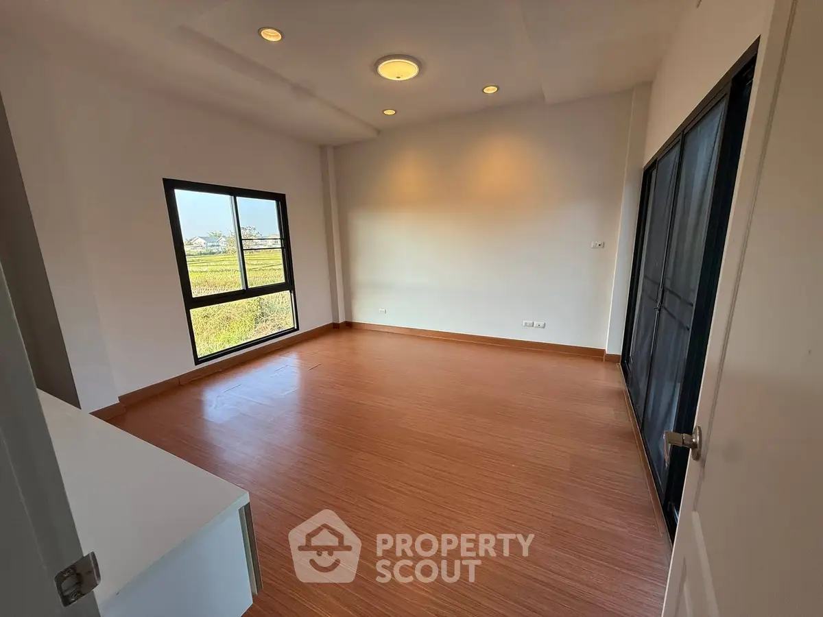 Spacious empty room with wooden flooring and large window offering scenic views.