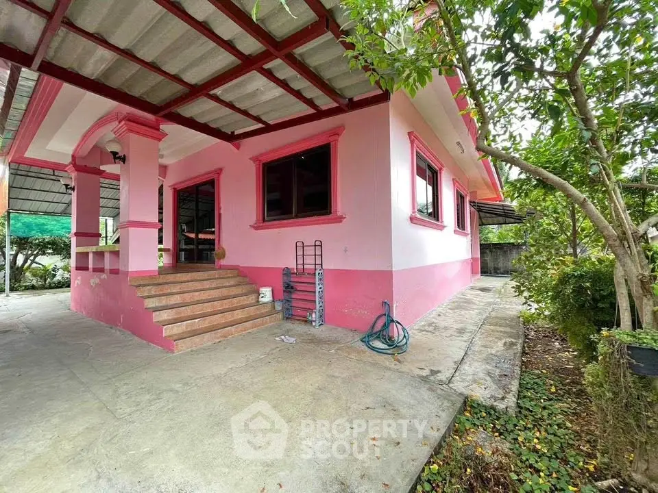 Charming pink house exterior with lush greenery and spacious patio area.