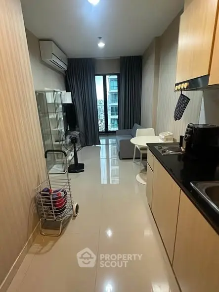 Modern apartment with open kitchen and cozy living area, featuring sleek cabinetry and large window with city view.