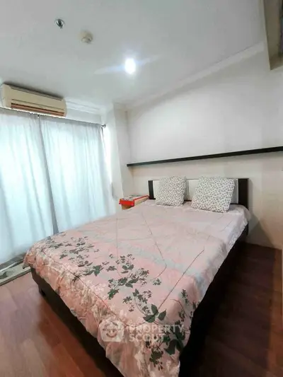Cozy bedroom with wooden flooring and natural light, featuring a comfortable bed and modern air conditioning.