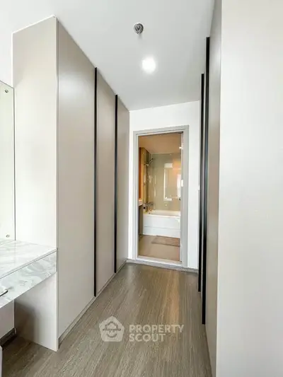 Modern hallway leading to a sleek bathroom with a bathtub, featuring elegant cabinetry and bright lighting.