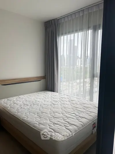 Bright bedroom with large window and city view, featuring a comfortable mattress and modern design.