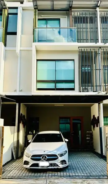 Modern townhouse exterior with car parked in driveway, showcasing sleek design and large windows.