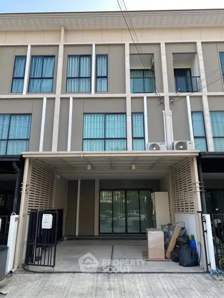 Modern three-story townhouse with large windows and covered parking area, ideal for urban living.