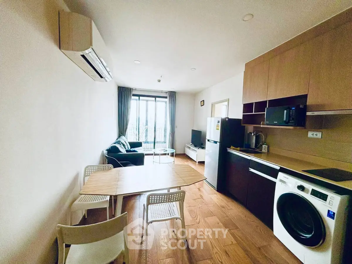 Modern living room with open kitchen, featuring washing machine and stylish furniture.
