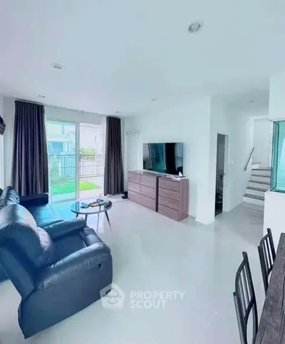 Modern living room with sleek furniture and large TV, open to garden view.
