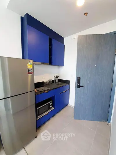 Modern compact kitchen with blue cabinets and stainless steel appliances in a stylish apartment.