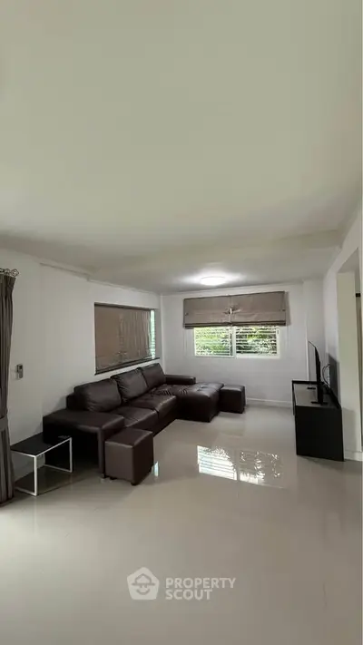 Spacious living room with modern brown leather sectional sofa and large windows for natural light.