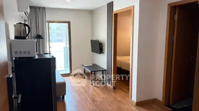 Modern apartment interior with wooden flooring, cozy living area, and natural light from balcony.