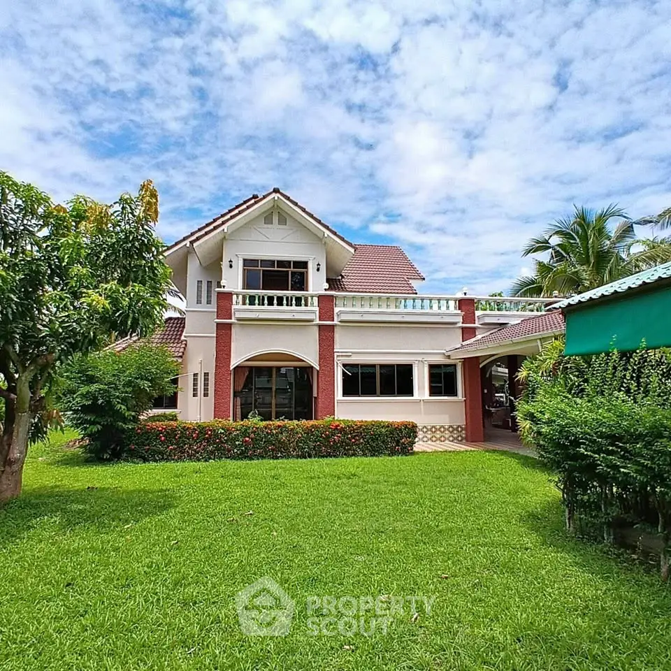 Charming two-story house with lush garden and spacious lawn under a clear blue sky.