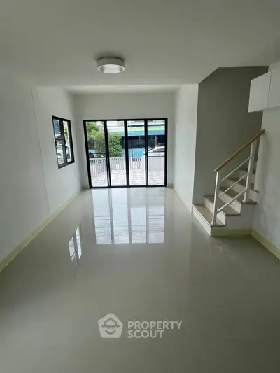 Spacious empty living room with large windows and staircase, ideal for customization.