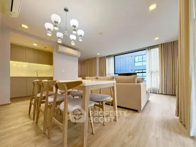 Spacious modern living room with open kitchen and elegant dining area, featuring stylish lighting and large windows.