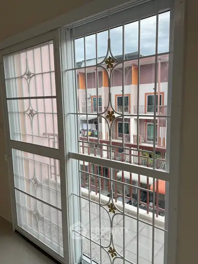 Spacious apartment window with decorative security bars offering a view of colorful urban buildings.