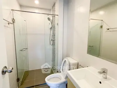 Modern bathroom with glass shower enclosure, sleek white fixtures, and well-lit mirror creating a clean, minimalist aesthetic.