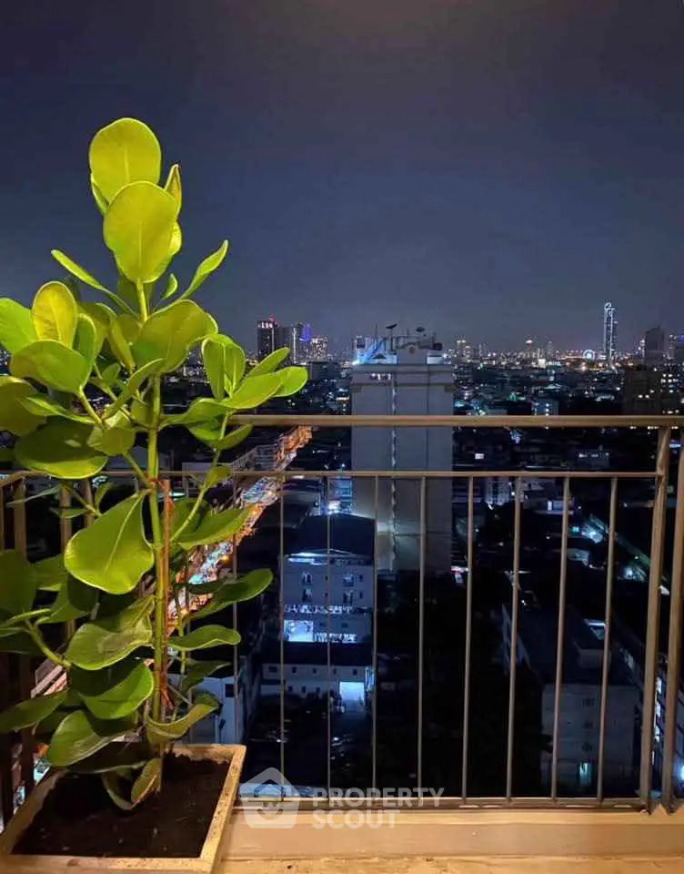 Stunning cityscape view from a high-rise balcony at night with lush green plant.