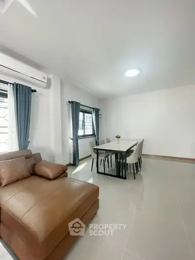 Modern living room with brown leather sofa and dining area, bright and spacious.