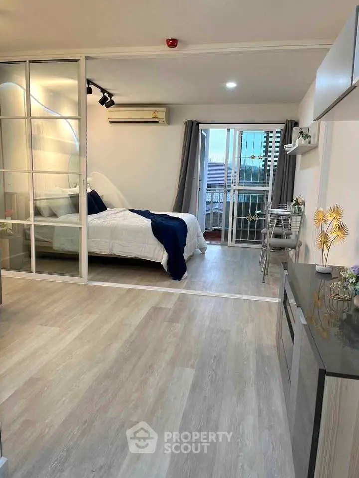 Modern studio apartment with glass partition, cozy bed, and balcony view.