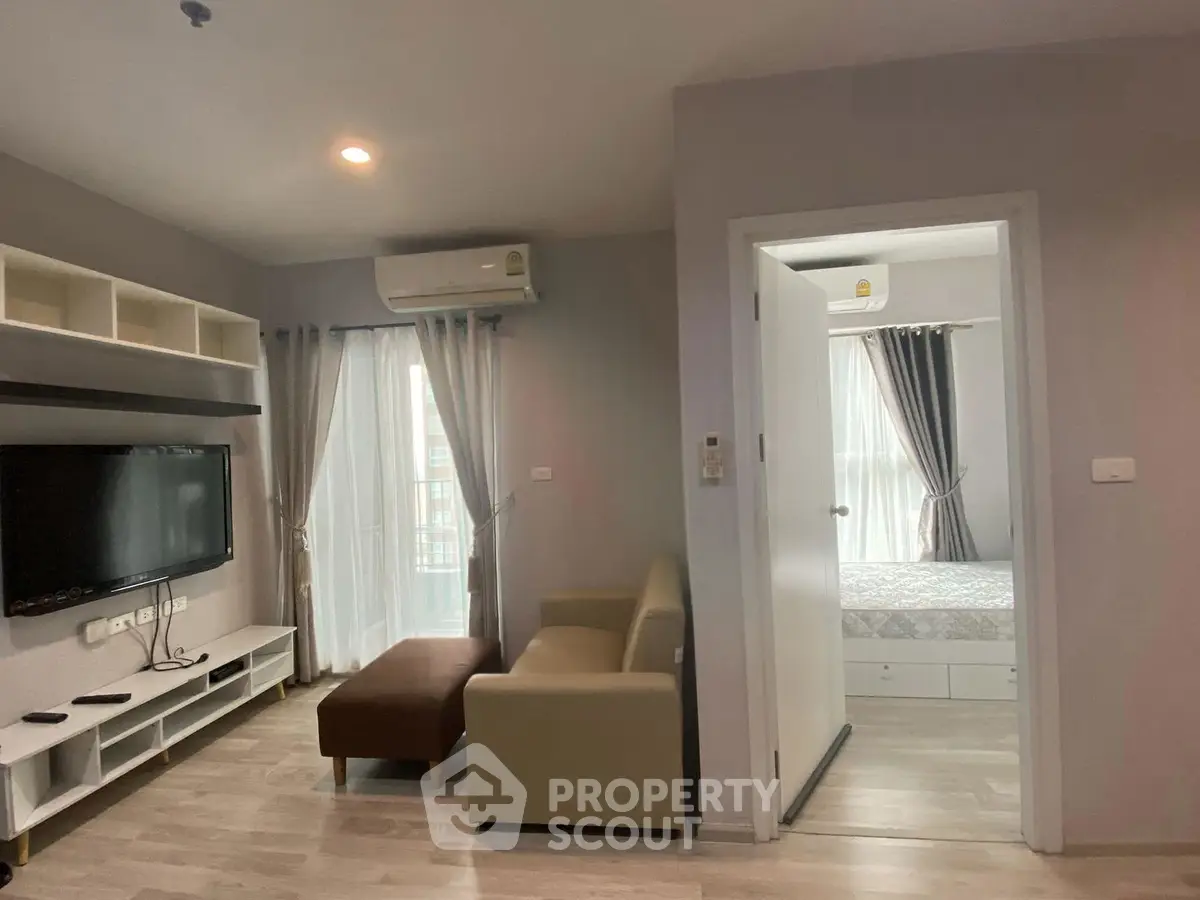 Modern apartment living room with TV and cozy sofa, adjacent to a bright bedroom.