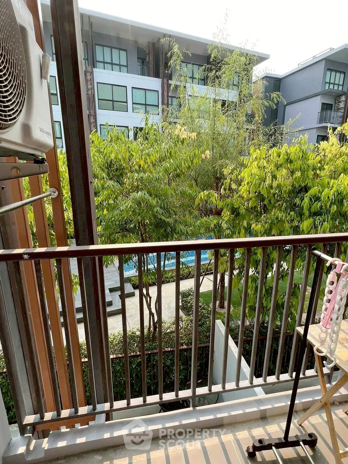 Charming balcony view overlooking lush greenery and modern apartment complex, perfect for relaxation.