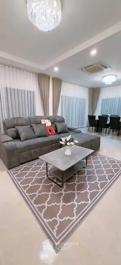 Spacious living room with elegant decor and dining area, featuring a plush gray sofa and modern chandelier.