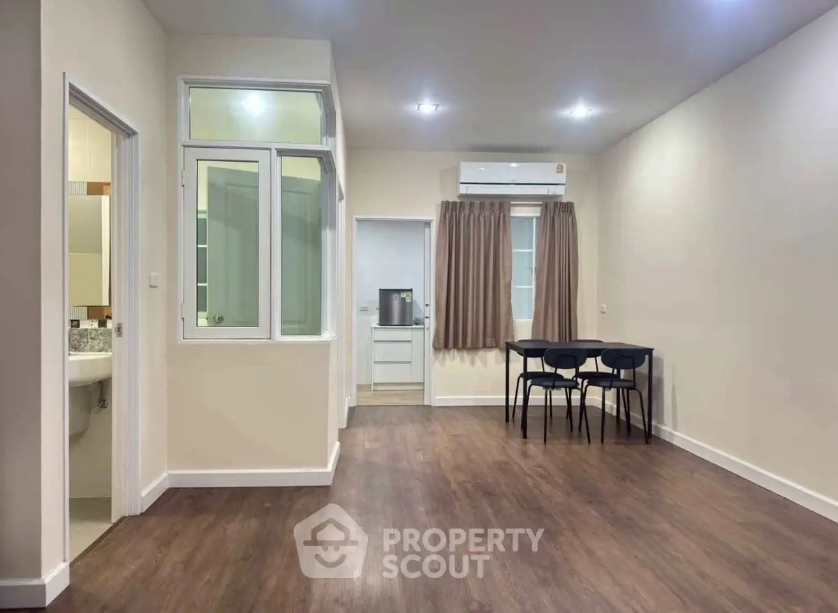 Spacious open-plan living area with modern wood flooring and dining space, featuring a compact kitchen and bathroom access.