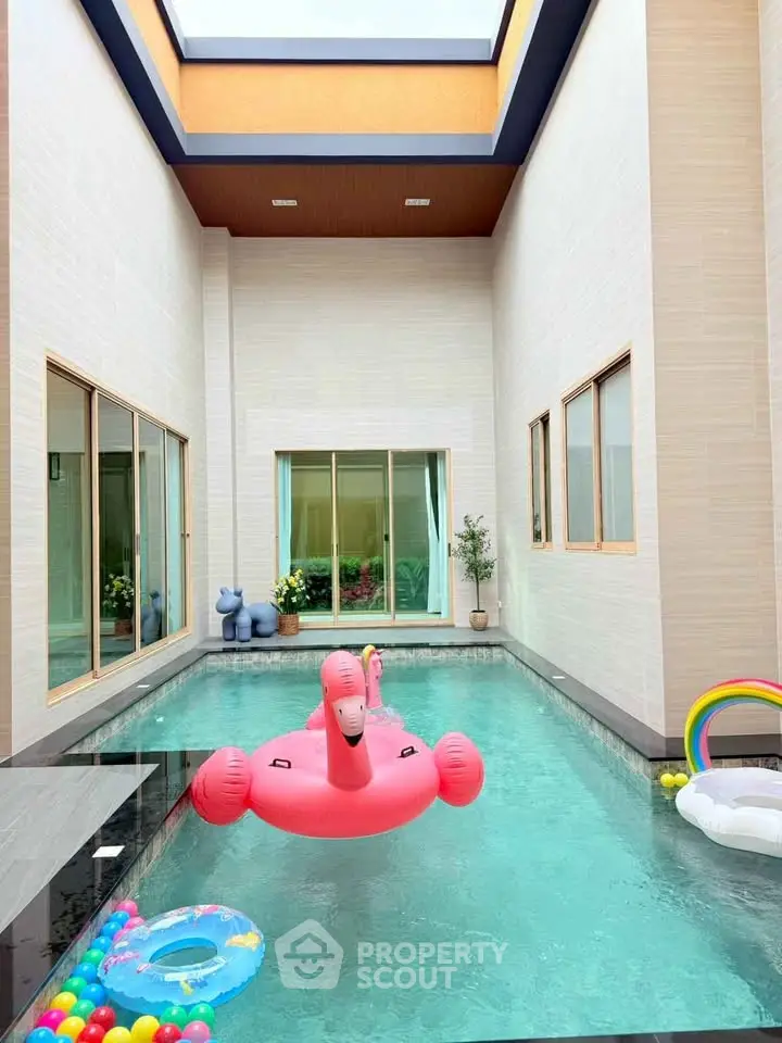 Luxurious indoor pool with playful floaties in modern home courtyard.