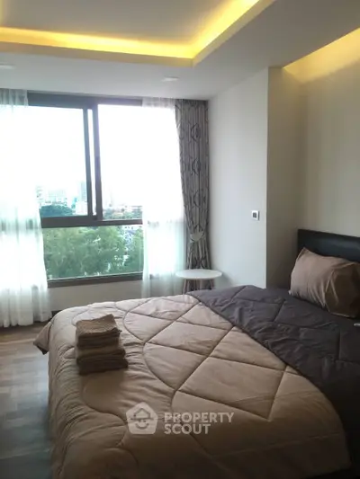 Modern bedroom with large window and cozy bedding in a high-rise apartment.
