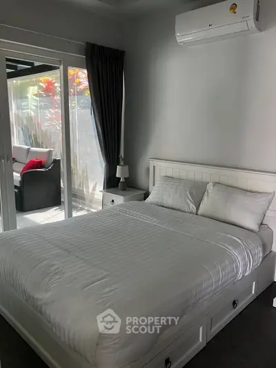 Cozy bedroom with white bedding and sliding glass doors leading to a patio with outdoor seating.