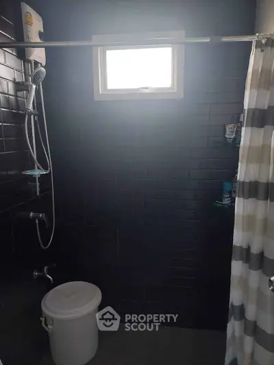 Modern bathroom with dark tiles and shower curtain, featuring a window for natural light.